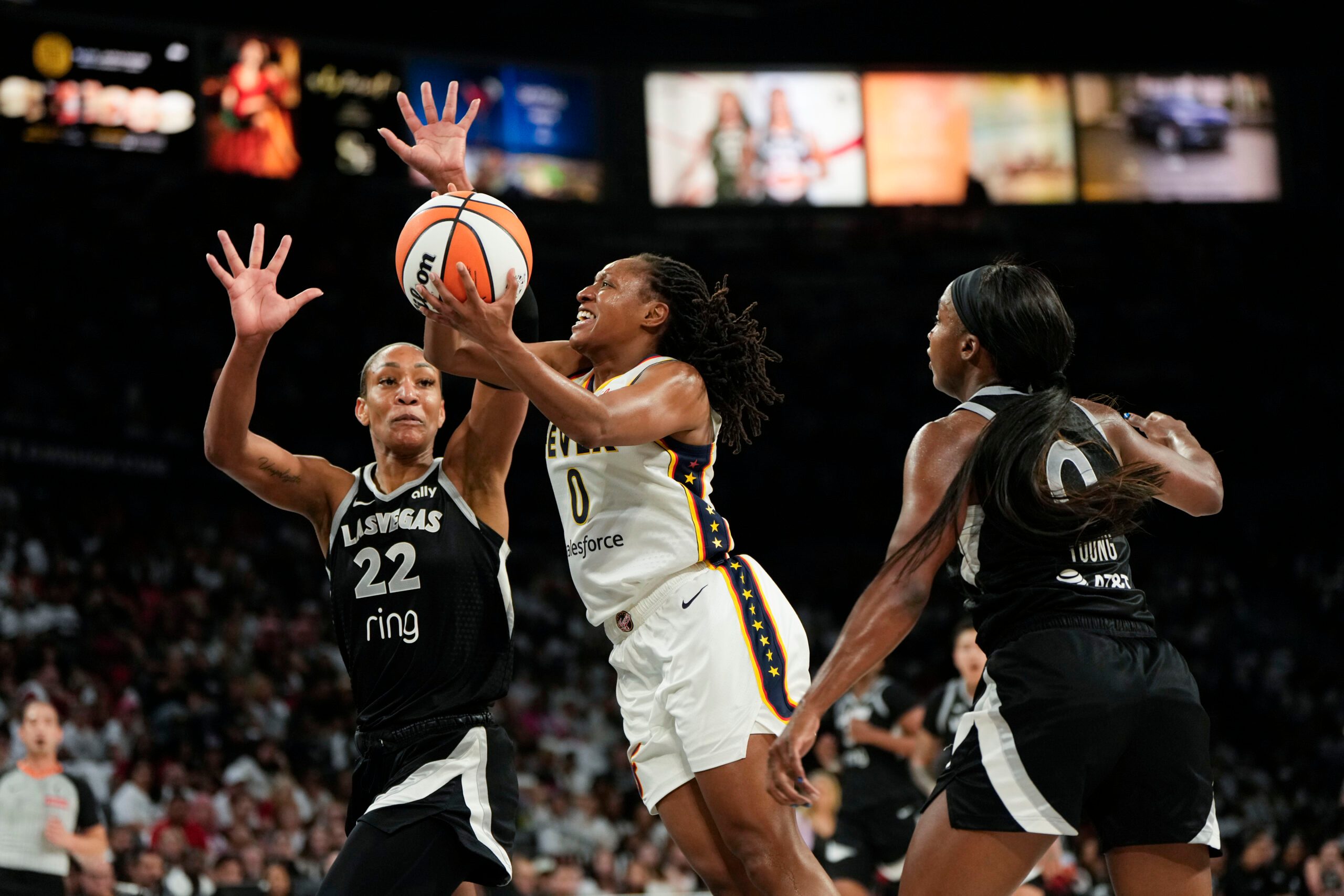 Sep 21, 2025; Las Vegas, Nevada, USA; Indiana Fever guard Kelsey Mitchell (0) attempts to score a layup against Las Vegas Aces center A'ja Wilson (22) and guard Jackie Young (0) during the second quarter in game one of the second round for the 2025 WNBA Playoffs at Michelob Ultra Arena. Mandatory Credit: Lucas Peltier-Imagn Images