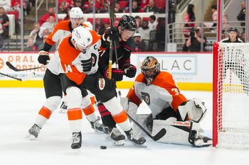Oct 11, 2025; Raleigh, North Carolina, USA;  Carolina Hurricanes defenseman Alexander Nikishin (21) and Philadelphia Flyers center Sean Couturier (14) battle over the loose puck in from of Philadelphia Flyers goaltender Samuel Ersson (33) during the third period at Lenovo Center. Mandatory Credit: James Guillory-Imagn Images