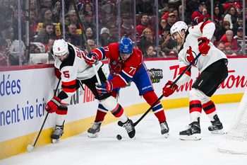 Feb 8, 2025; Montreal, Quebec, CAN; New Jersey Devils defenseman Brenden Dillon (5) and defenseman Dougie Hamilton (7) defend the puck against Montreal Canadiens center Kirby Dach (77) near the boards during the second period at Bell Centre. Mandatory Credit: David Kirouac-Imagn Images