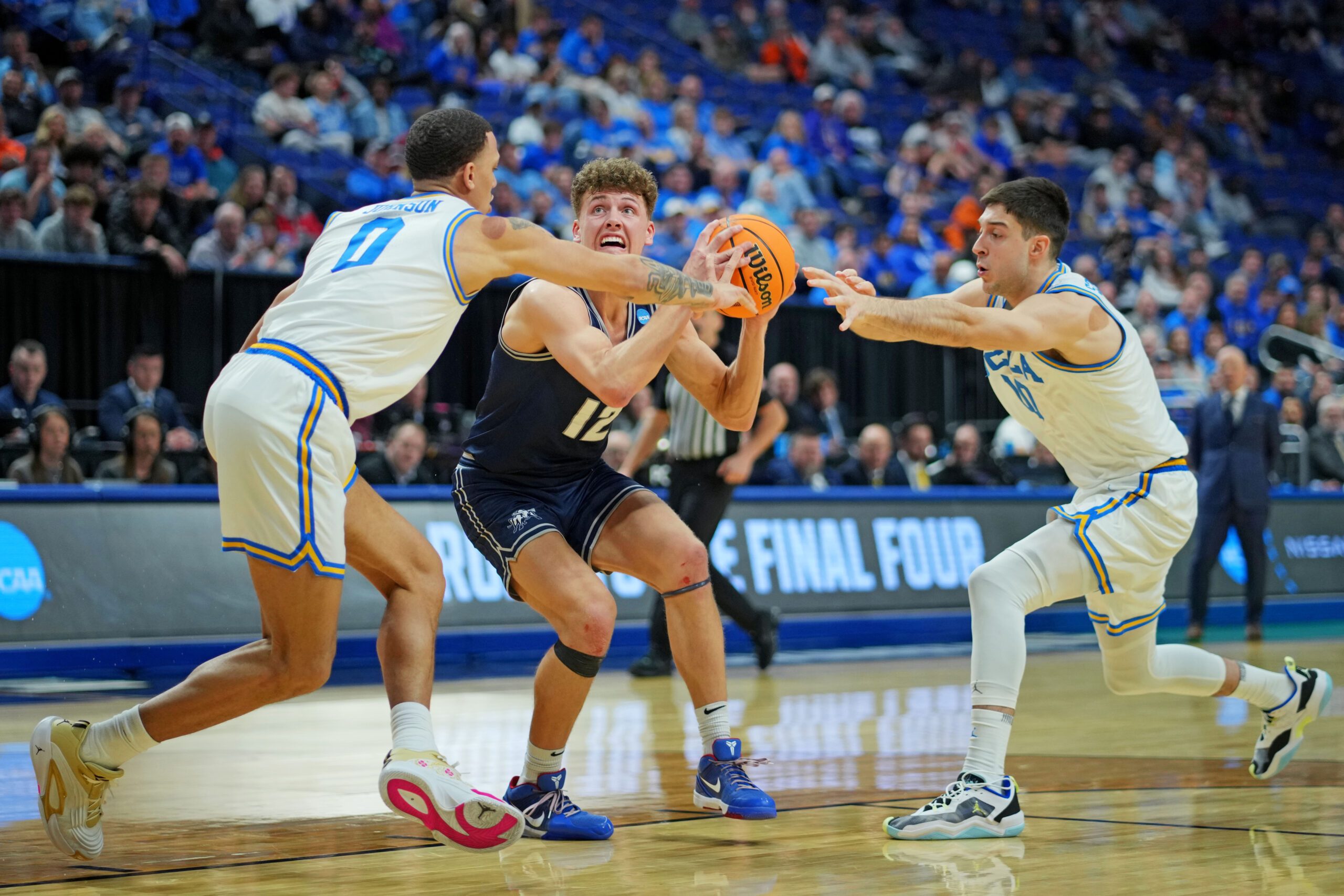 Mar 20, 2025; Lexington, KY, USA;  Utah State Aggies guard Mason Falslev (12) drives to the basket against UCLA Bruins guard Kobe Johnson (0) during the second half in the first round of the NCAA Tournament at Rupp Arena. Mandatory Credit: Aaron Doster-Imagn Images