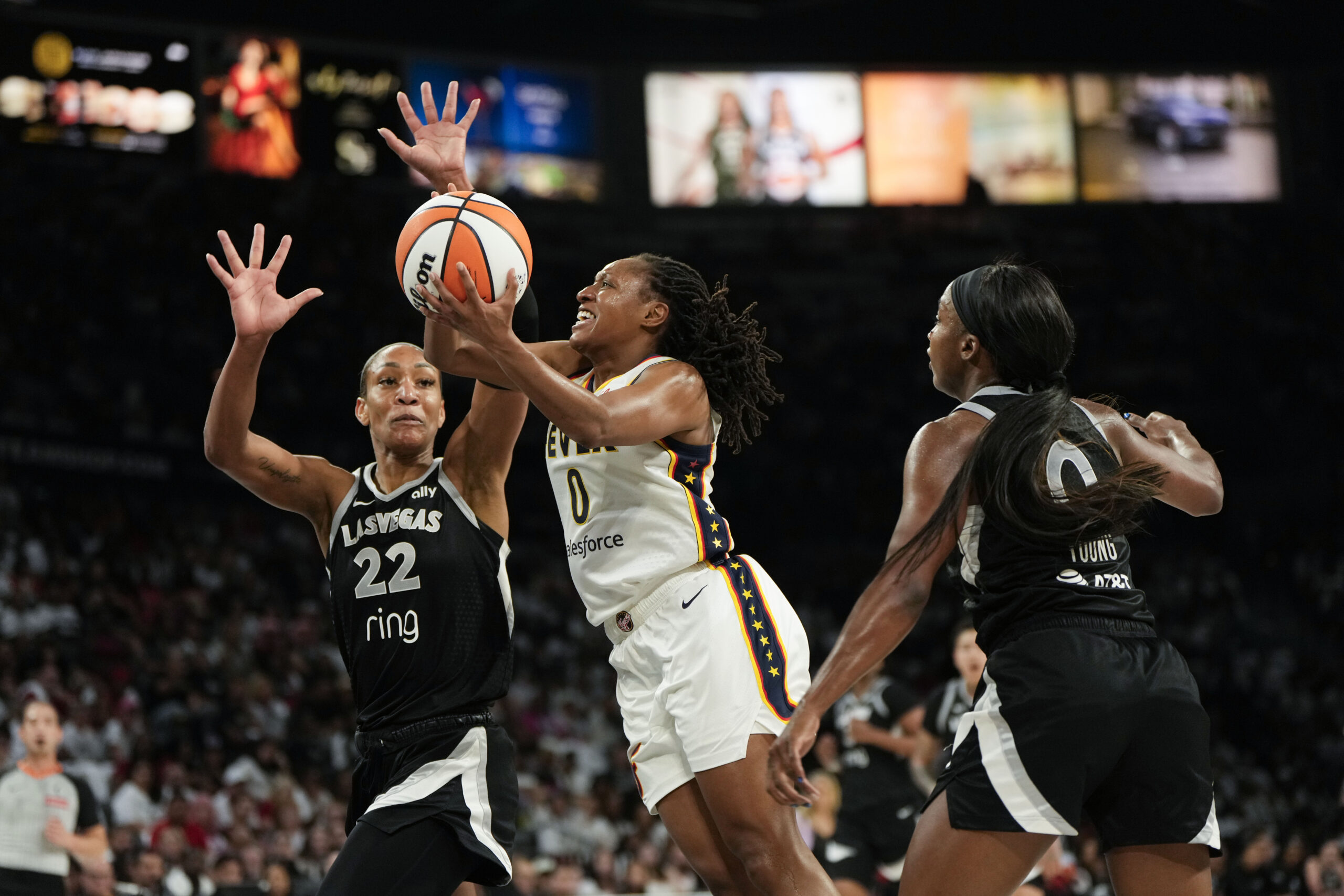 Sep 21, 2025; Las Vegas, Nevada, USA; Indiana Fever guard Kelsey Mitchell (0) attempts to score a layup against Las Vegas Aces center A'ja Wilson (22) and guard Jackie Young (0) during the second quarter in game one of the second round for the 2025 WNBA Playoffs at Michelob Ultra Arena. Mandatory Credit: Lucas Peltier-Imagn Images