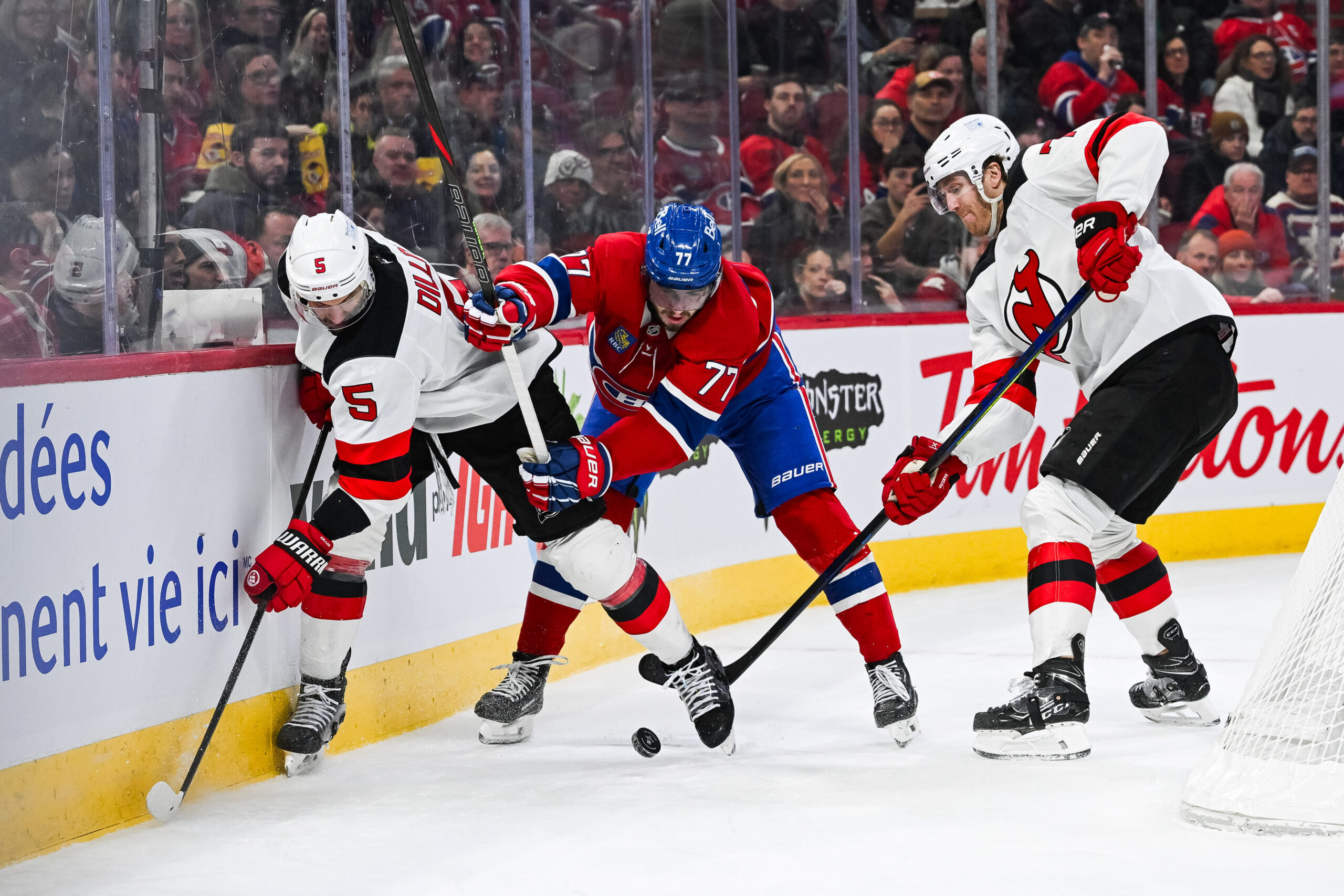 Feb 8, 2025; Montreal, Quebec, CAN; New Jersey Devils defenseman Brenden Dillon (5) and defenseman Dougie Hamilton (7) defend the puck against Montreal Canadiens center Kirby Dach (77) near the boards during the second period at Bell Centre. Mandatory Credit: David Kirouac-Imagn Images