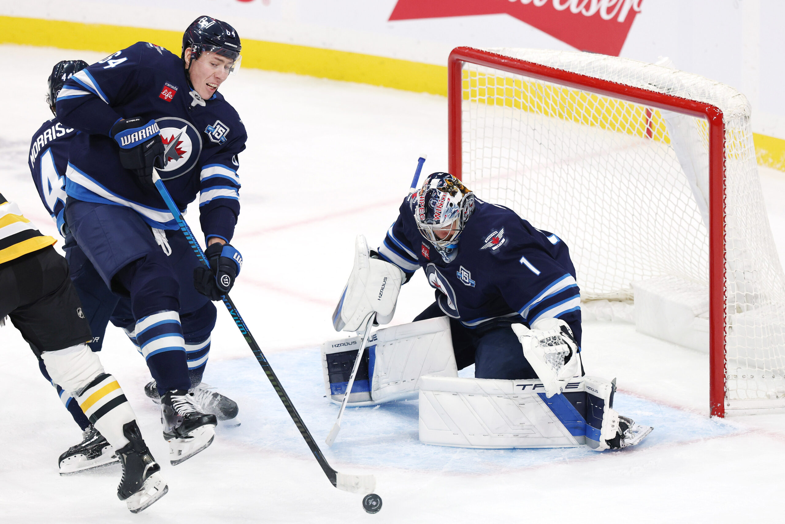 Nov 1, 2025; Winnipeg, Manitoba, CAN; Winnipeg Jets defenseman Logan Stanley (64) clears the puck away from goaltender Eric Comrie (1) during a game against the Pittsburgh Penguins in the third period at Canada Life Centre. Mandatory Credit: James Carey Lauder-Imagn Images